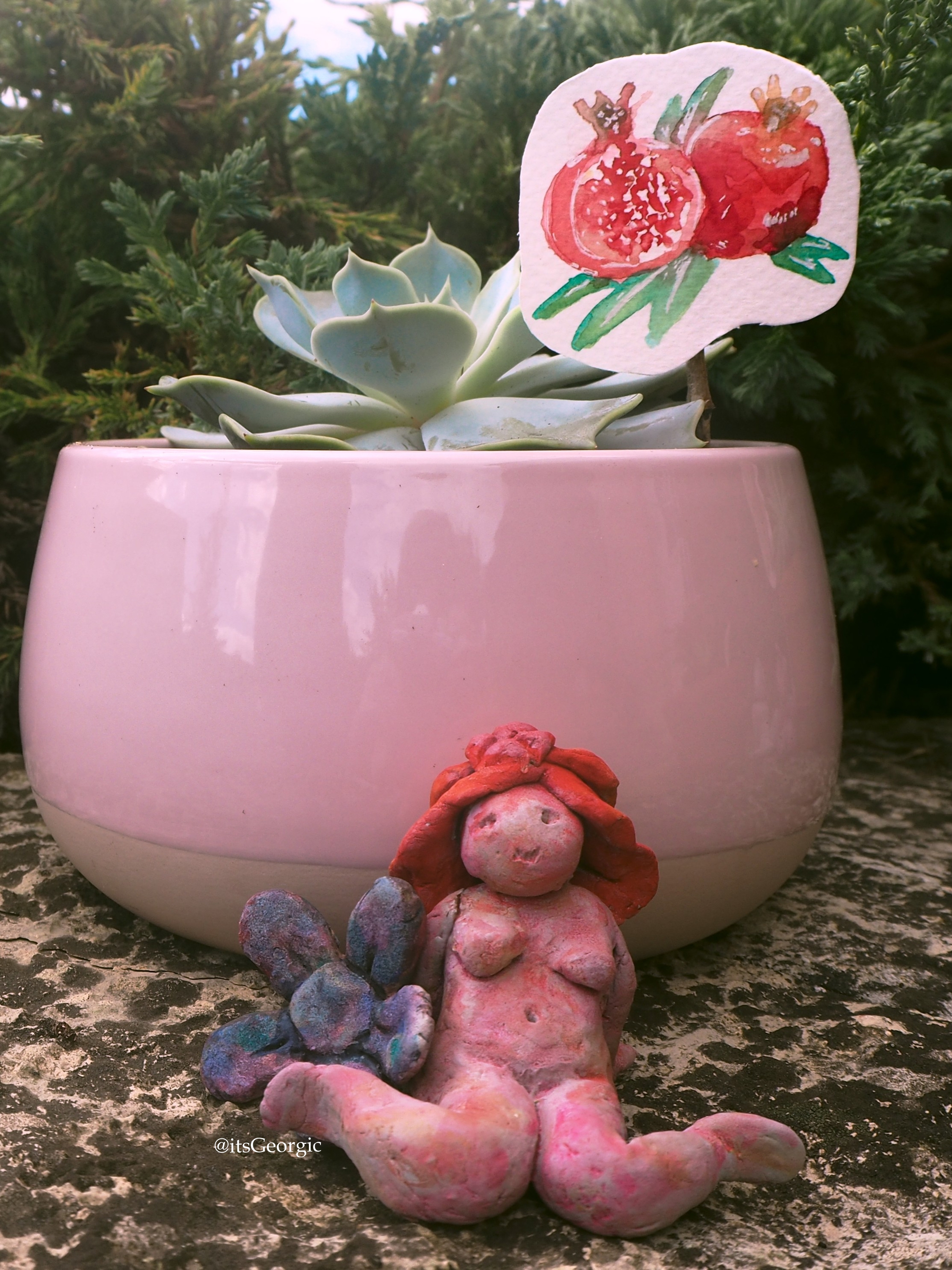 Photo de la statuette de Perséphone devant un pot rose contenant une succulente (echeveria lilacina) et un dessin à l'aquarelle d'une grenade ouverte.