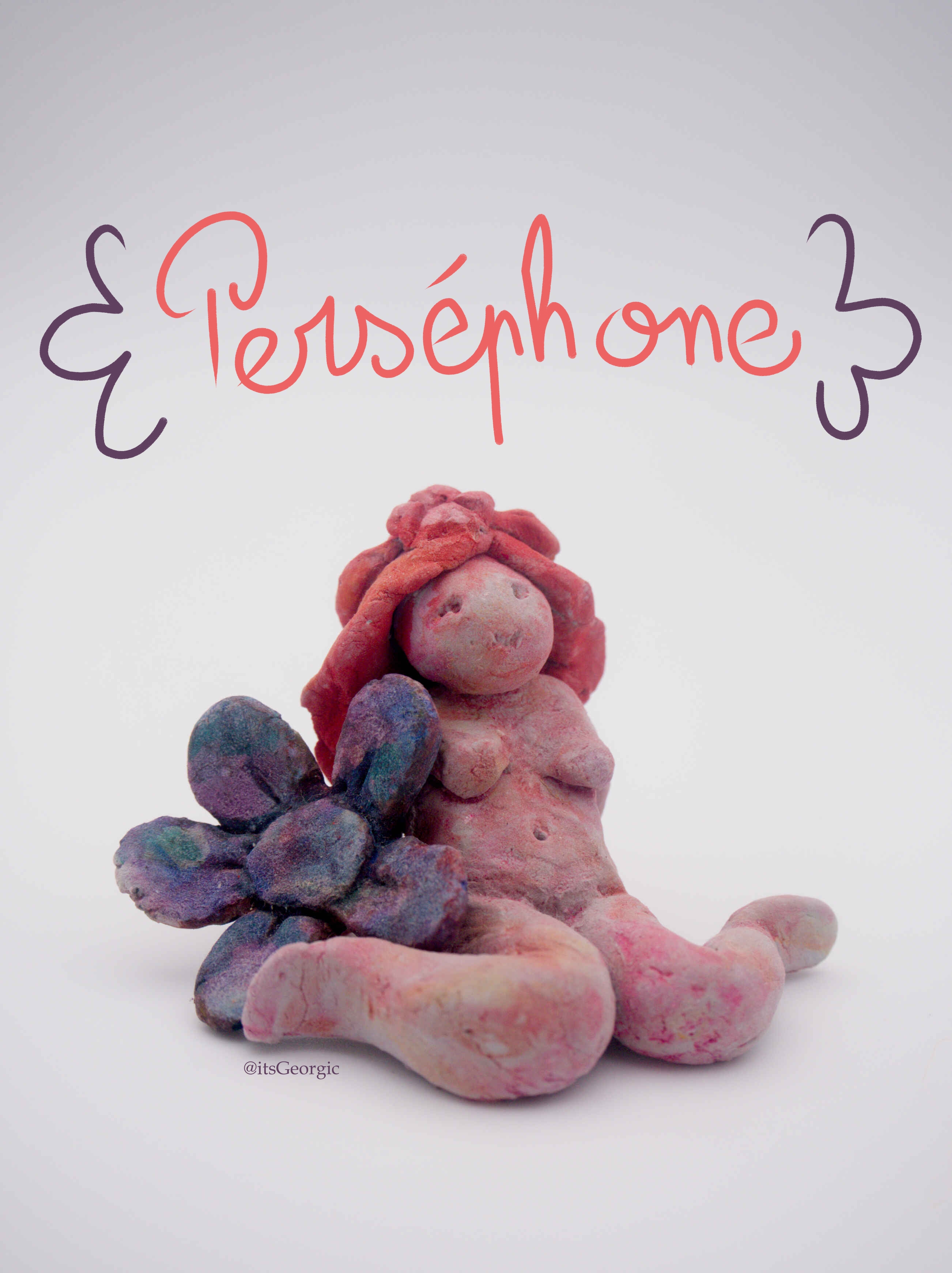 Photo d'une statuette d'une femme assise les genoux en W avec une grosse fleur violette contre elle. La statue a les cheveux longs et est peinte en rose avec un effet aquarelle.