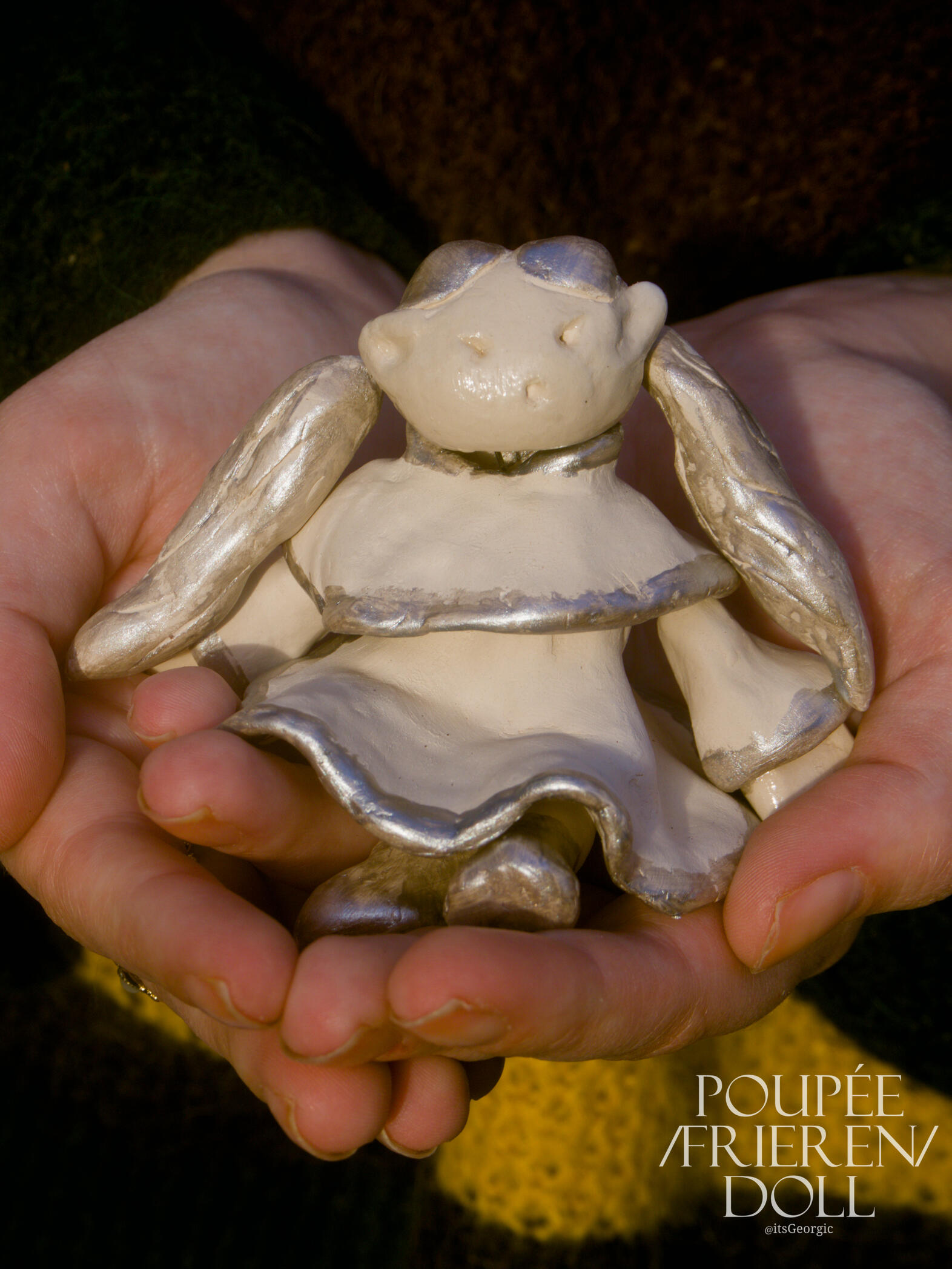 Photo de la poupée Frieren tenue dans les paumes de deux mains. Elle est lovée dans le creux des mains.