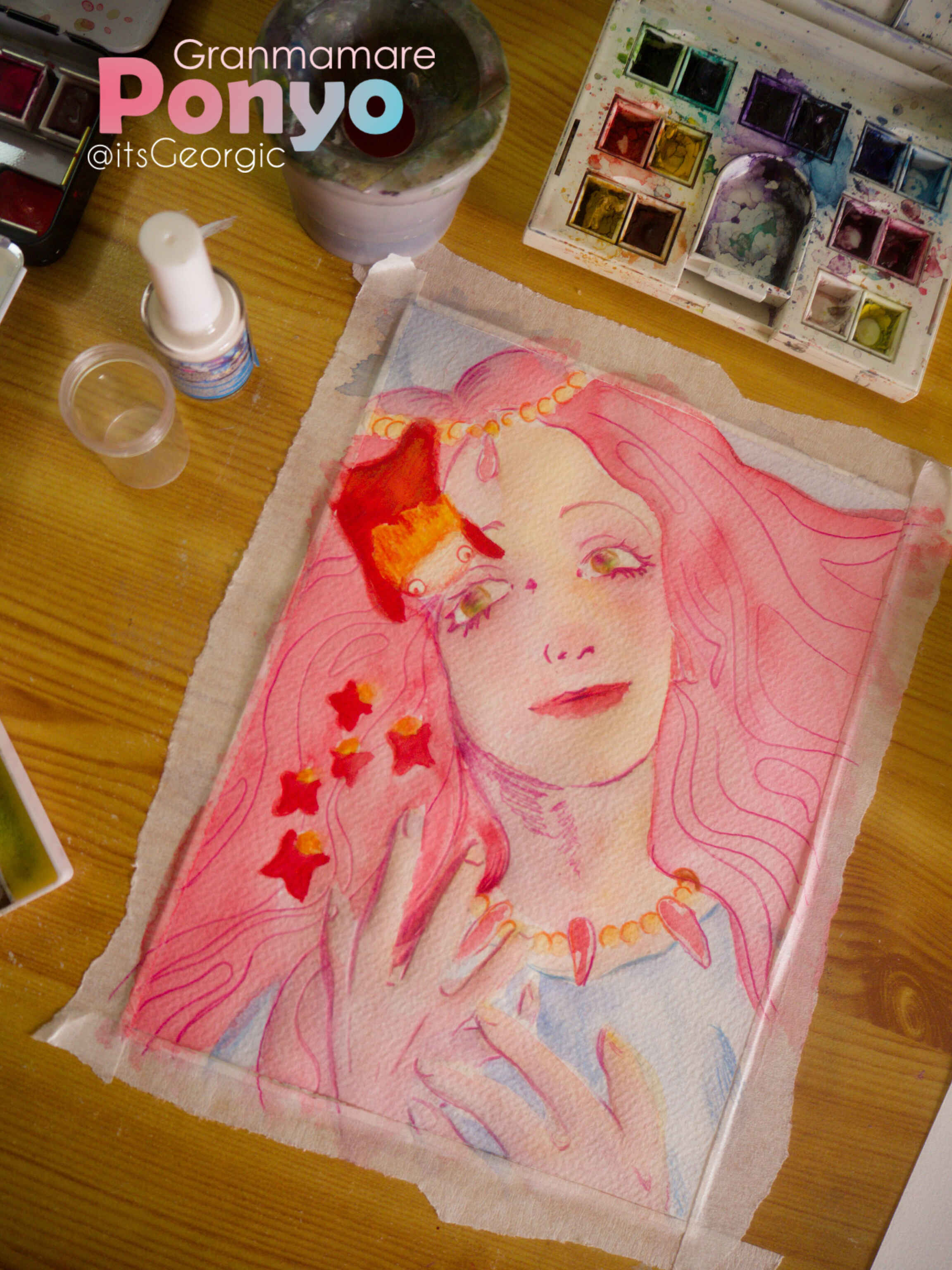 Photo de l'œuvre en cours de réalisation collée à une planche, avec des palettes d'aquarelle, de la colle, et d'autres outils à côté d'elle.