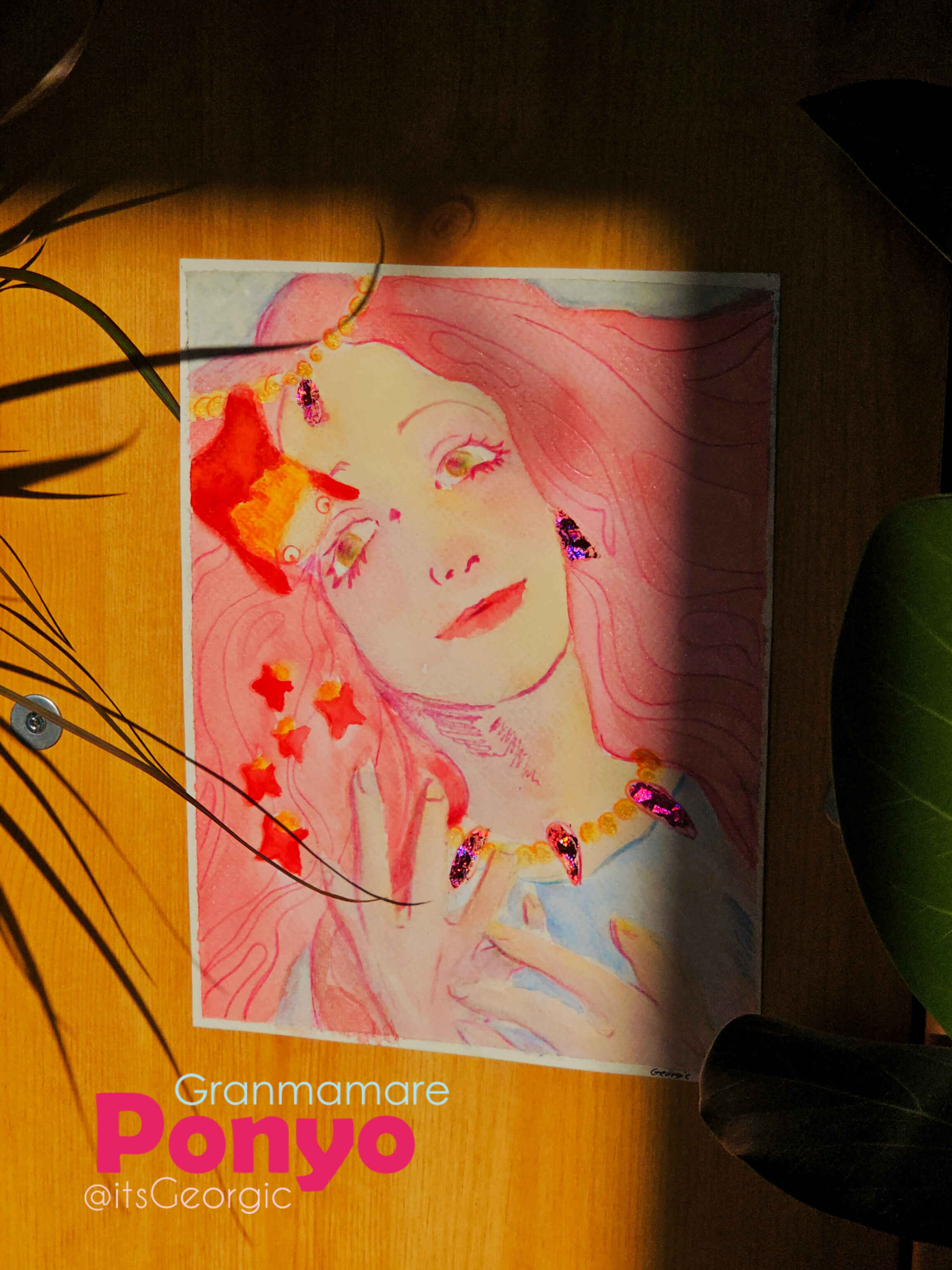 Photo de l'oeuvre accrochée sur le côté d'un meuble au soleil de sorte que l'on voit les reflets des paillettes et des feuilles irisées.